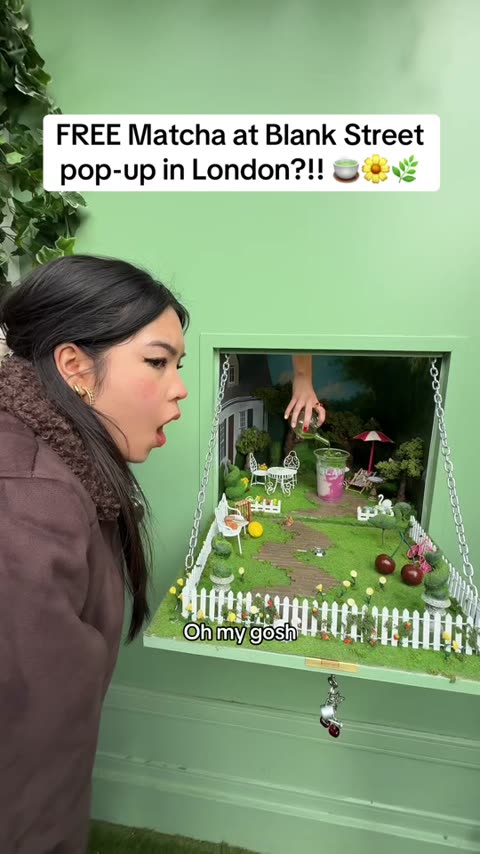Blank Street London pop-up pickup window built as a miniature garden diorama; a hand reaches in from above placing the matcha cup; creator gasps.